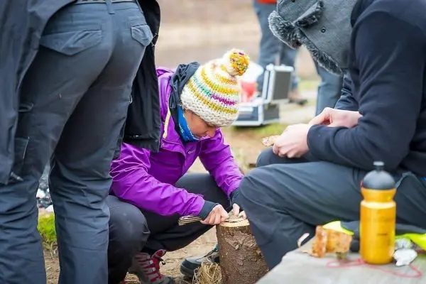 Person bearbeitet Holzstück mit Werkzeug beim Überlebenstraining