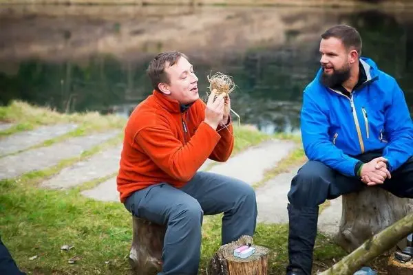 Person hält Zunder in der Hand und spricht mit einer anderen Person beim Survival Training