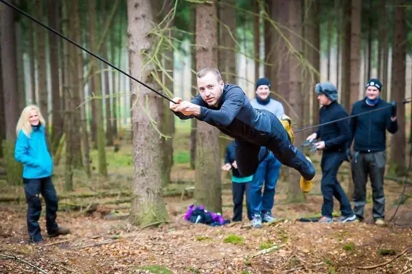 Person schwingt an Seil zwischen Bäumen, Gruppe beobachtet
