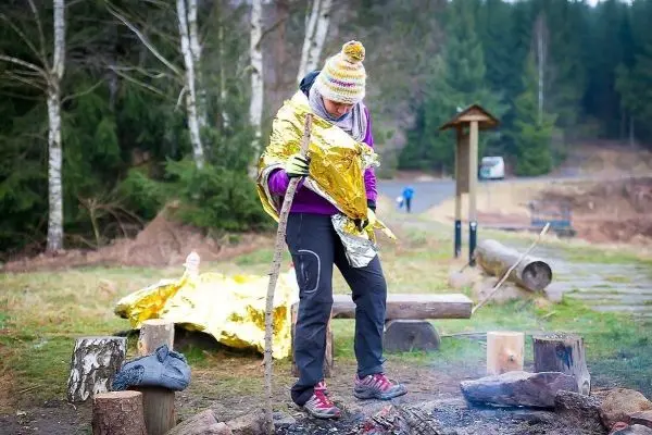 Person steht neben einem kleinen Feuer und hält einen Stock in der Hand
