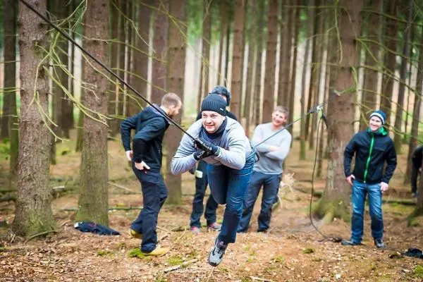 Person überquert selbstgebaute Seilbrücke im Wald, andere beobachten