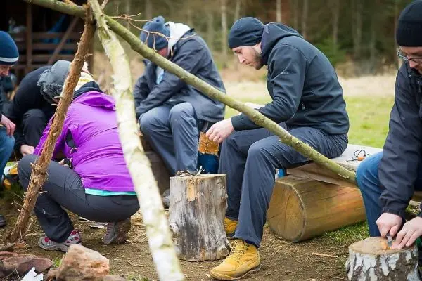 Teilnehmer bearbeiten Holzstücke auf Baumstämmen in einer Gruppenaktivität
