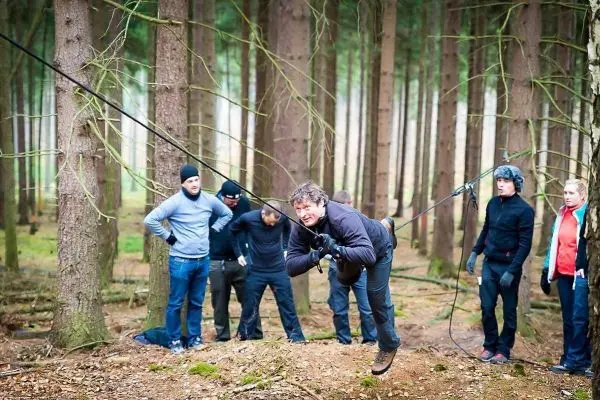 Teilnehmer überquert eine selbstgebaute Seilbrücke im Wald