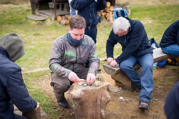 Zunder wird auf einem Baumstumpf vorbereitet, während Teilnehmer um ihn herum sitzen