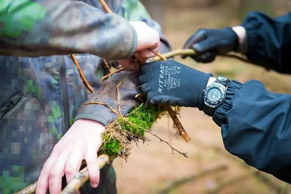 Zwei Hände binden einen Stock mit Moos und Rinde zusammen