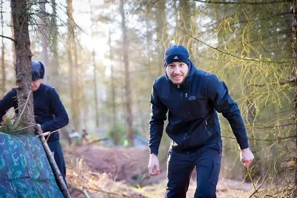 Zwei Personen arbeiten im Wald an einer Tarp-Notunterkunft