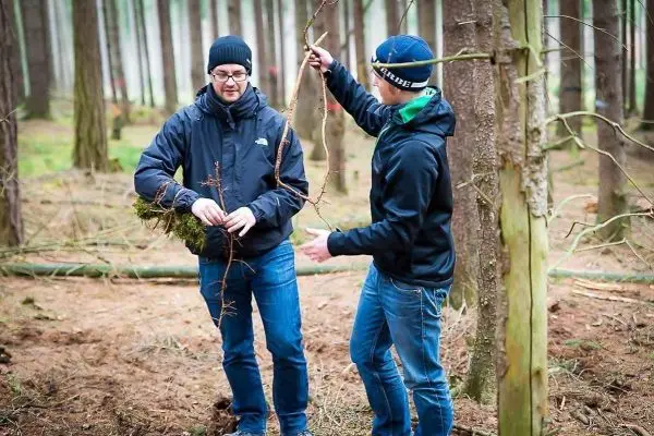 Zwei Personen halten Äste und Moos im Wald