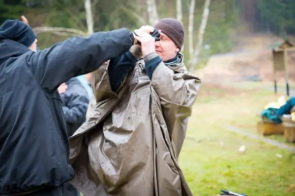 Zwei Personen helfen sich beim Anziehen eines wasserdichten Überwurfs