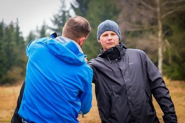 Zwei Personen in Outdoor-Bekleidung führen eine Übung zur Selbstverteidigung durch
