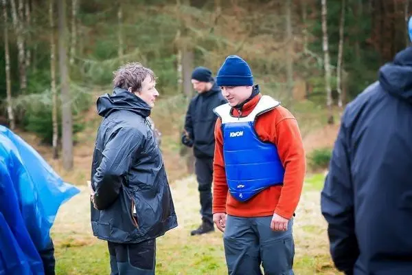 Zwei Personen in wetterfester Kleidung stehen im Gespräch, im Hintergrund weitere Teilnehmer