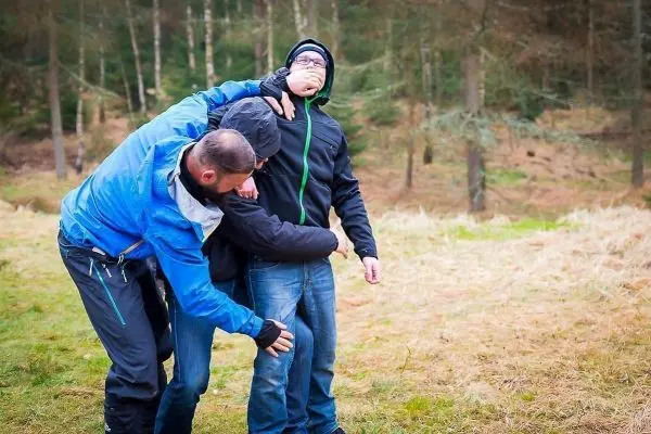 Zwei Personen üben eine Kontrollestechnik an einer dritten Person im Freien aus