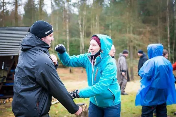 Zwei Personen üben eine Technik im Freien, während andere im Hintergrund stehen