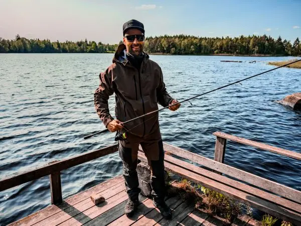Angler hält Angelrute auf einer Holzplattform am Wasser
