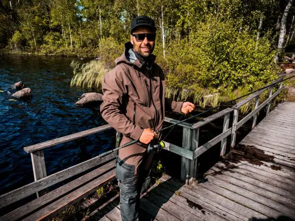 Angler hält Angelrute auf Holzsteg am Wasser, umgeben von Bäumen