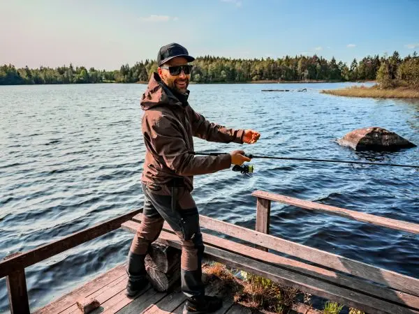 Angler steht auf Holzsteg und hält Angelrute über Wasserfläche