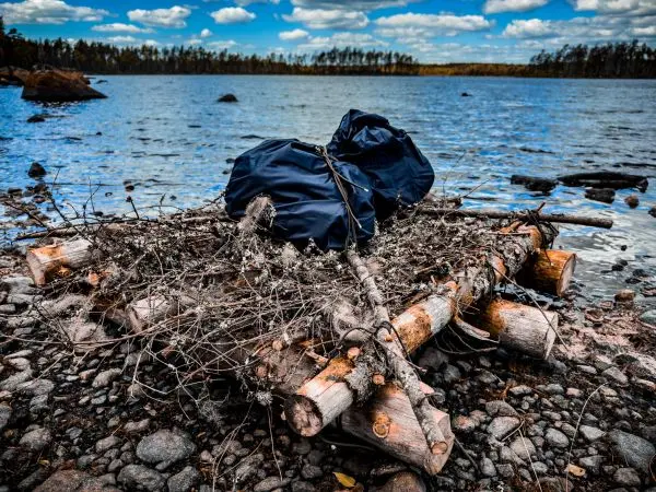 Ein Rucksack liegt auf einem Holzstapel am Wasser
