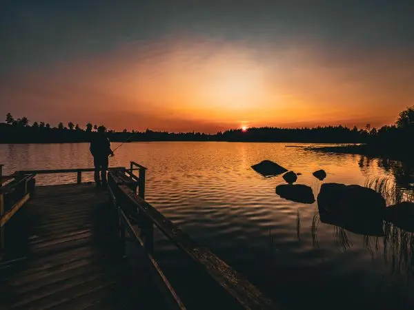 Fischer steht auf einem Holzsteg und angelt in ruhigem Wasser bei Sonnenuntergang