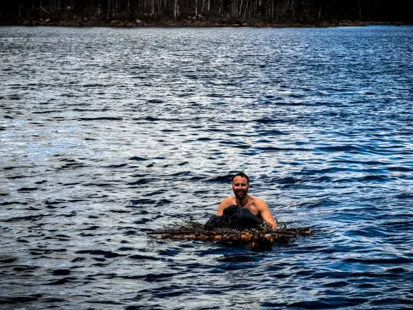 Mann schwimmt auf einem improvisierten Floß aus Ästen im Wasser