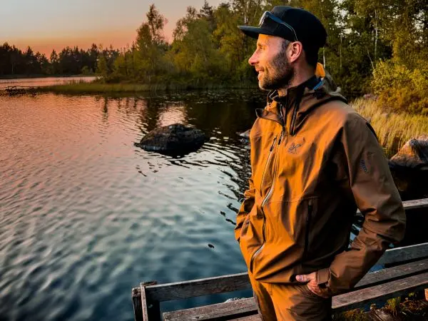 Mann steht an einem Holzsteg und blickt auf einen See bei Sonnenuntergang