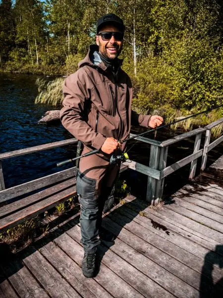Mann steht auf Holzsteg am Wasser und hält Angelrute in der Hand