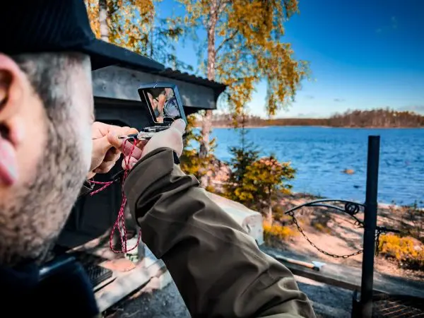 Person hält ein Smartphone und fotografiert eine Landschaft am Wasser