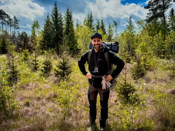 Person steht lächelnd im Wald mit Rucksack