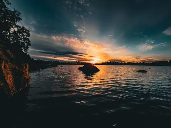 Sonnenuntergang über einem ruhigen Gewässer mit Felsen im Vordergrund