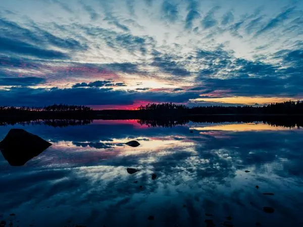 Wasseroberfläche spiegelt Wolken und Sonnenuntergang in ruhiger Landschaft