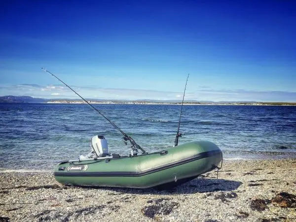 Auf einem Kiesstrand liegt ein grünes Schlauchboot mit zwei Angelruten