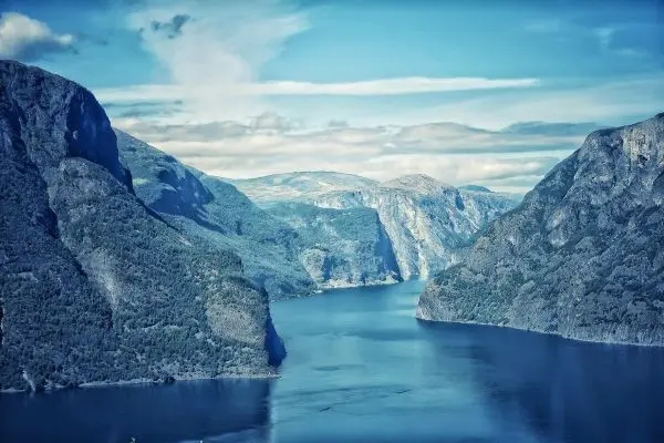 Berglandschaft mit Fjord und bewaldeten Hängen unter blauem Himmel