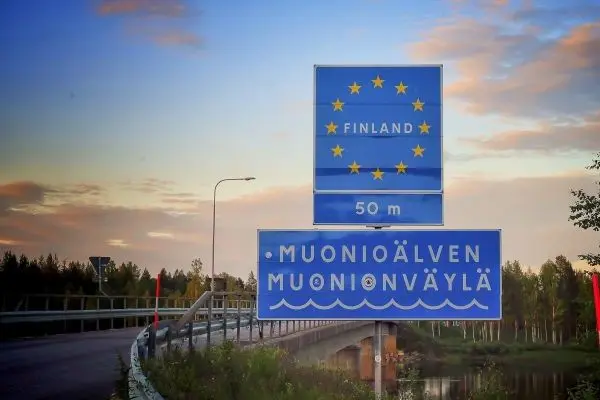Blaues Verkehrsschild mit EU-Sternen und Ortsnamen an einer Brücke über einen Fluss
