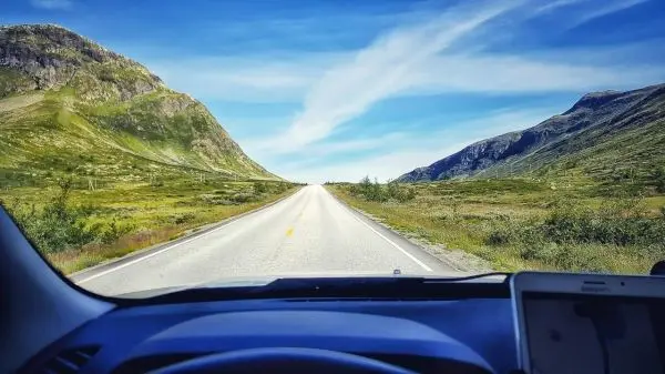 Blick auf eine gerade Straße zwischen grünen Hügeln und Bergen