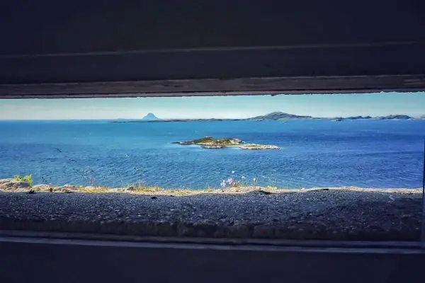 Blick durch einen schmalen Spalt auf eine Küstenlandschaft mit Inseln und Wasser