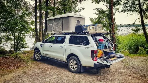 Campingfahrzeug mit Dachzelt und Ausrüstung am Ufer eines Gewässers