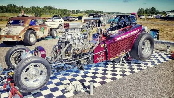 Dragster mit offenem Motor und breiten Reifen auf einem schwarz-weißen Schachbrettmuster