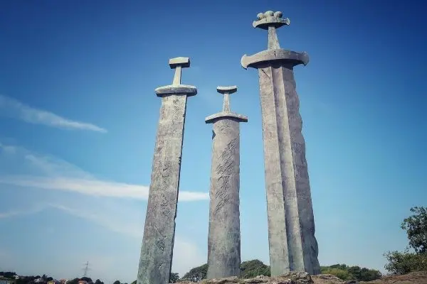 Drei große, stilisierte Schwertskulpturen aus Metall stehen auf einem Felsen