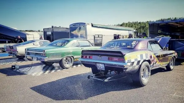 Drei Rennwagen stehen auf einer Rennstrecke, im Hintergrund sind Transportanhänger sichtbar