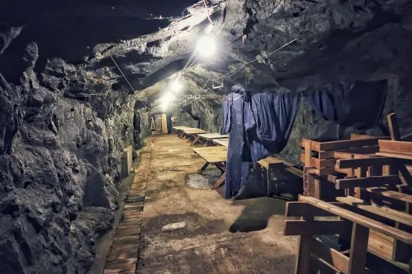 Dunkler Stollen mit Holzregalen und hängenden Vorhängen, beleuchtet von Deckenlampen
