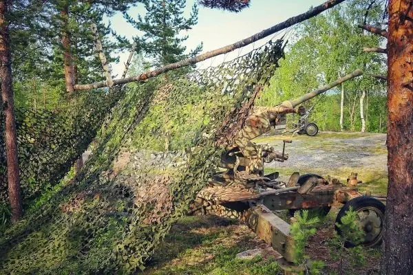 Ein camouflage Netz verdeckt eine alte Kanone zwischen Bäumen