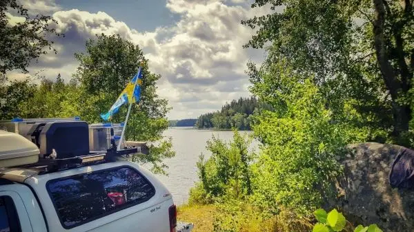 Ein Fahrzeug steht am Ufer eines Gewässers, umgeben von Bäumen und Felsen