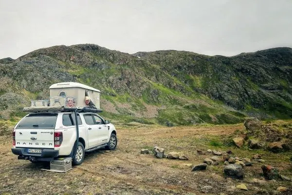 Ein geländegängiger Pickup mit Dachzelt steht auf einer Wiese vor einer Berglandschaft