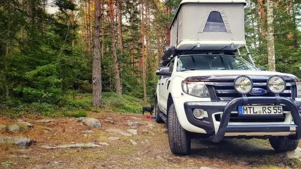 Geländewagen mit Dachzelt steht auf einem Waldweg zwischen Bäumen