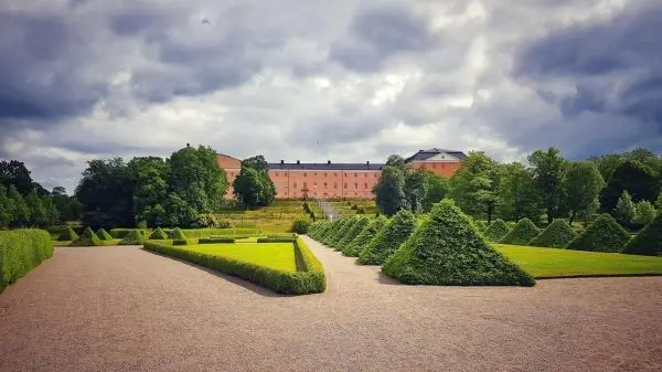 Gepflasterte Gartenanlage mit geometrischen Hecken und historischem Gebäude im Hintergrund