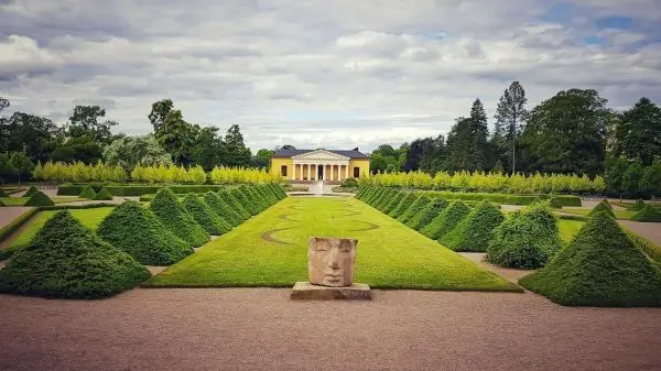 Gepflasterter Garten mit geometrischen Hecken und einem Skulpturenkopf im Vordergrund