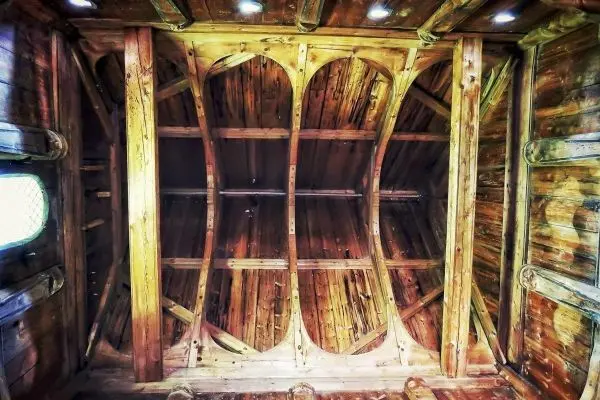 Holzdecke mit sichtbaren Balken und Rundungen, beleuchtet von integrierten Lichtern