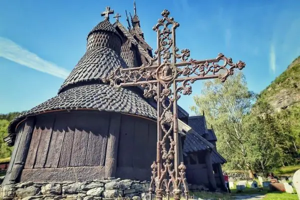 Holzkirche mit charakteristischer Dachkonstruktion und schmiedeeisernem Kreuz im Vordergrund