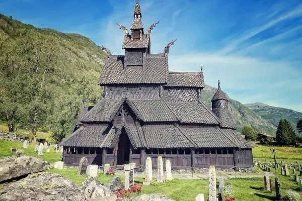 Holzkirche mit spitzen Dächern und umliegendem Friedhof in grüner Landschaft