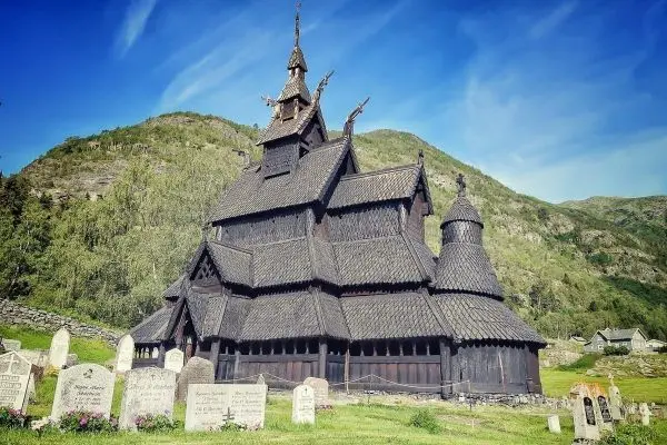 Holzkirche mit spitzen Dächern und umliegenden Grabsteinen in einer grünen Landschaft