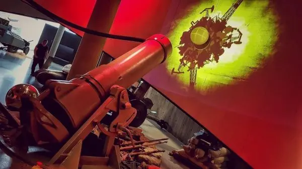 Kanone steht auf dem Boden, Schattenprojektion an der Wand zeigt ein technisches Motiv