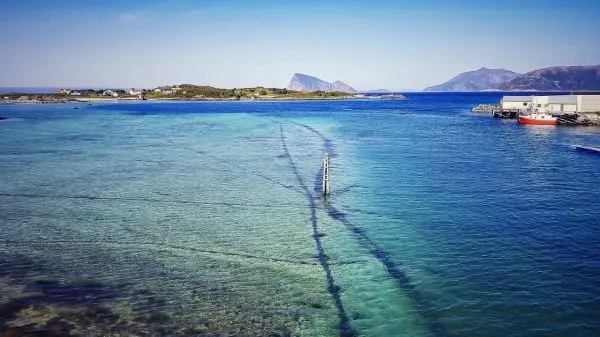Klares Wasser mit sichtbaren Spuren und einem Pfahl im Vordergrund